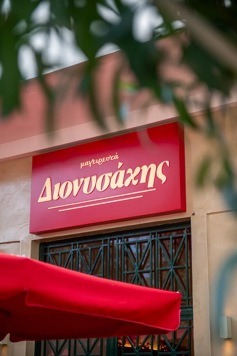 Η κόκκινη πινακίδα «μαγειρευτά Διονυσάκης» πάνω από την είσοδο του μαγαζιού